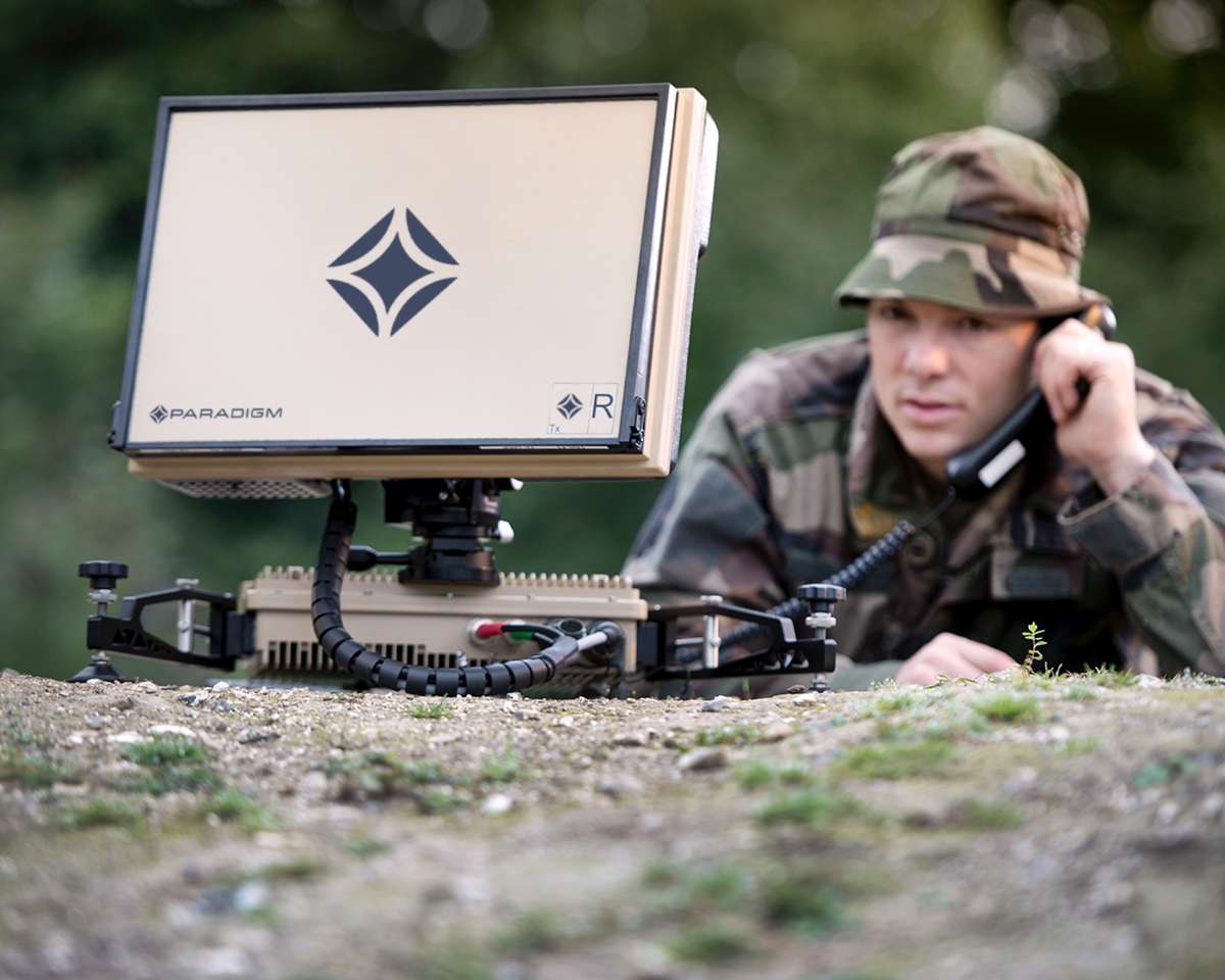 soldier with a handheld radio looking at a laptop